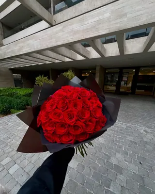 Ramo de rosas rojas entregado en mano frente a la entrada de un edificio